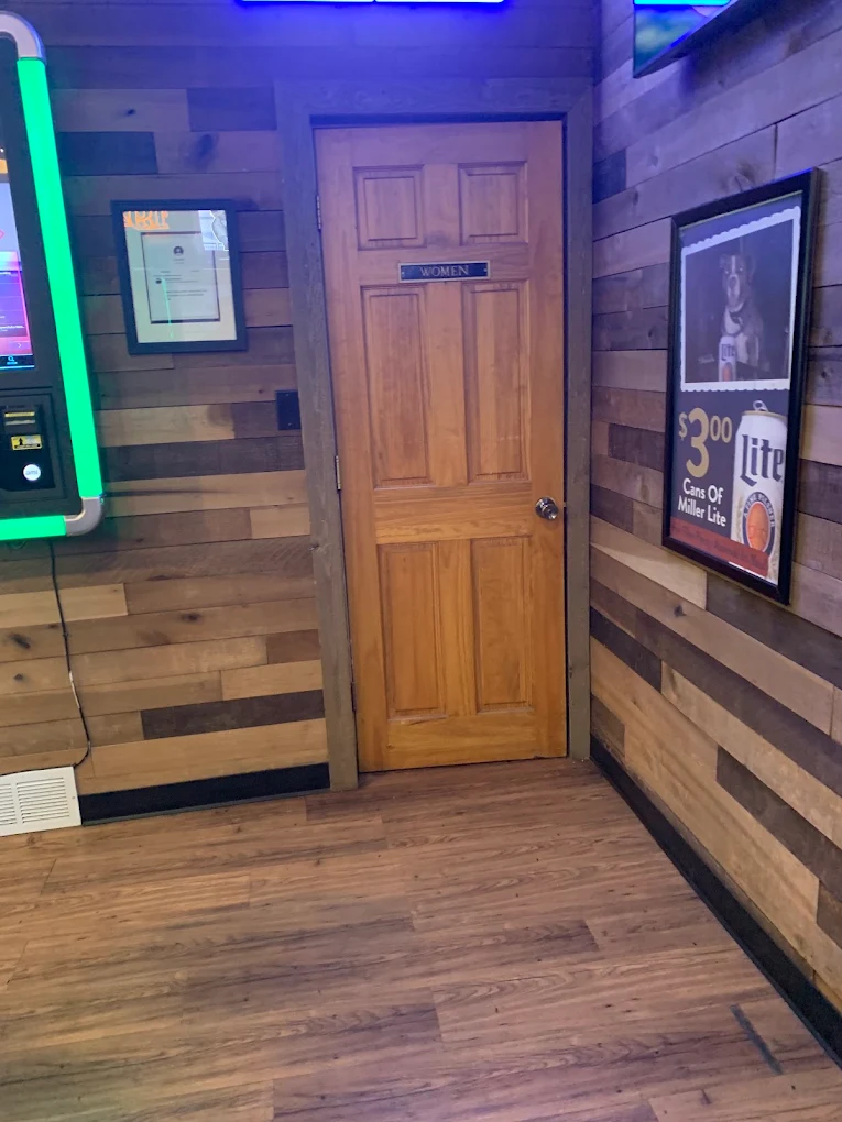 Wood-panelled back hallway at The Destination lit by green neon beside a gaming machine