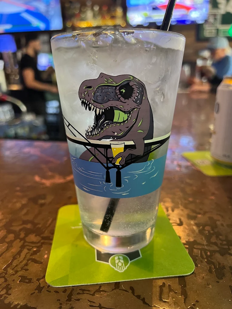 Tall cocktail in a dinosaur-print pint glass on the copper bar top