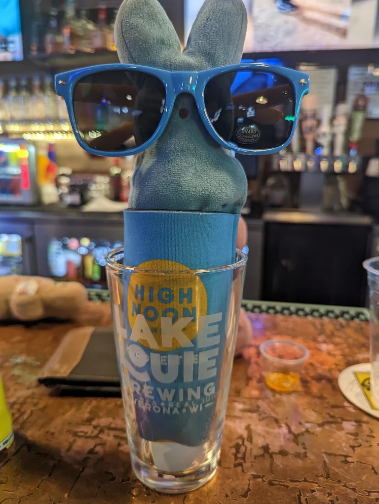 Plush Peeps bunny mascot wearing sunglasses, propped in a pint glass on the copper bar top